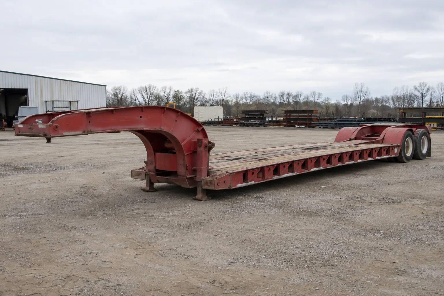 Empty red lowboy equipment trailer in an industrial yard