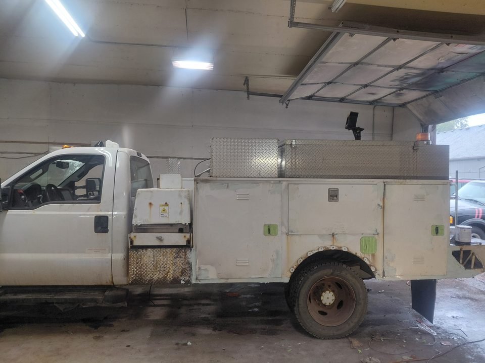 Before view of the F-450 inside the shop, showing rust and wear on the white utility body